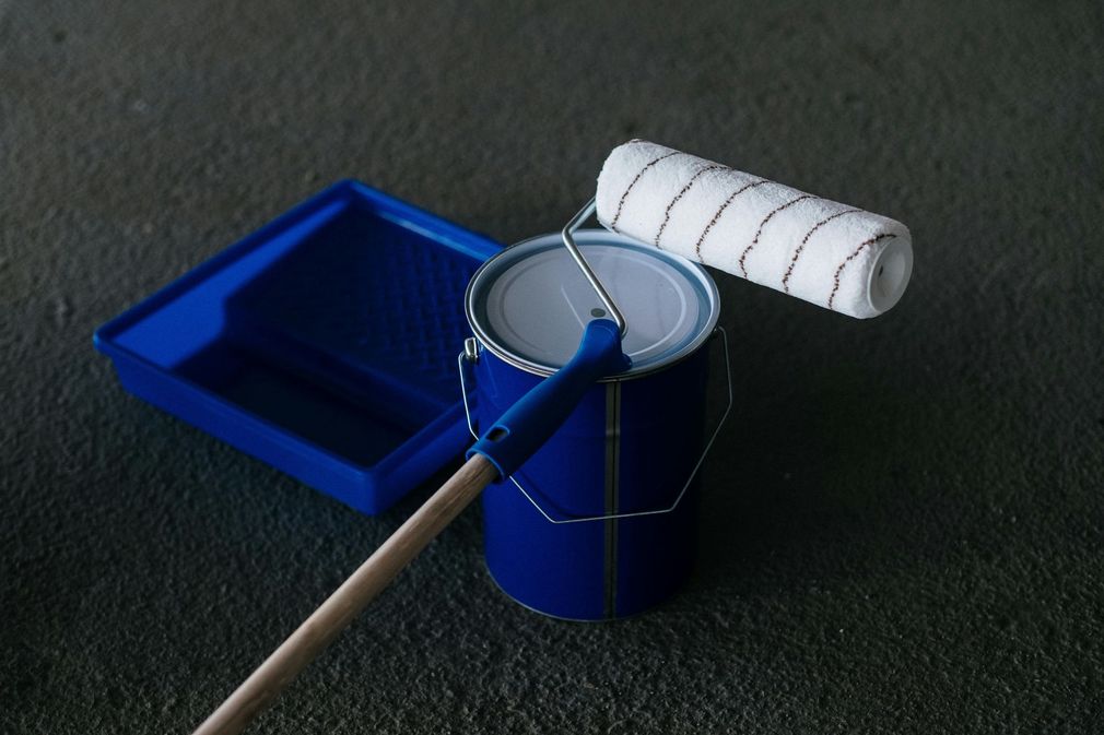 Paint roller resting in a blue paint tray and bucket on a dark surface