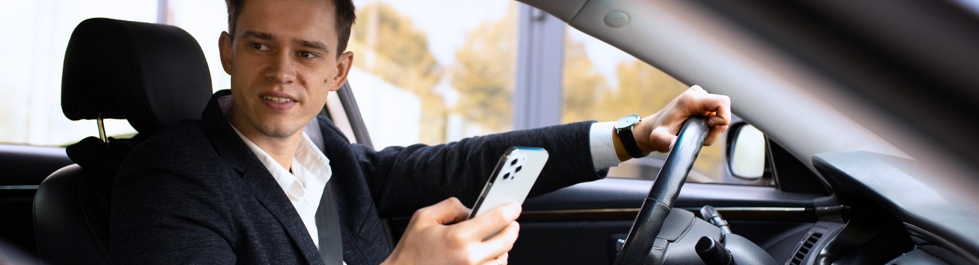 Homem dirigindo um carro enquanto segura um smartphone e olha para ele.