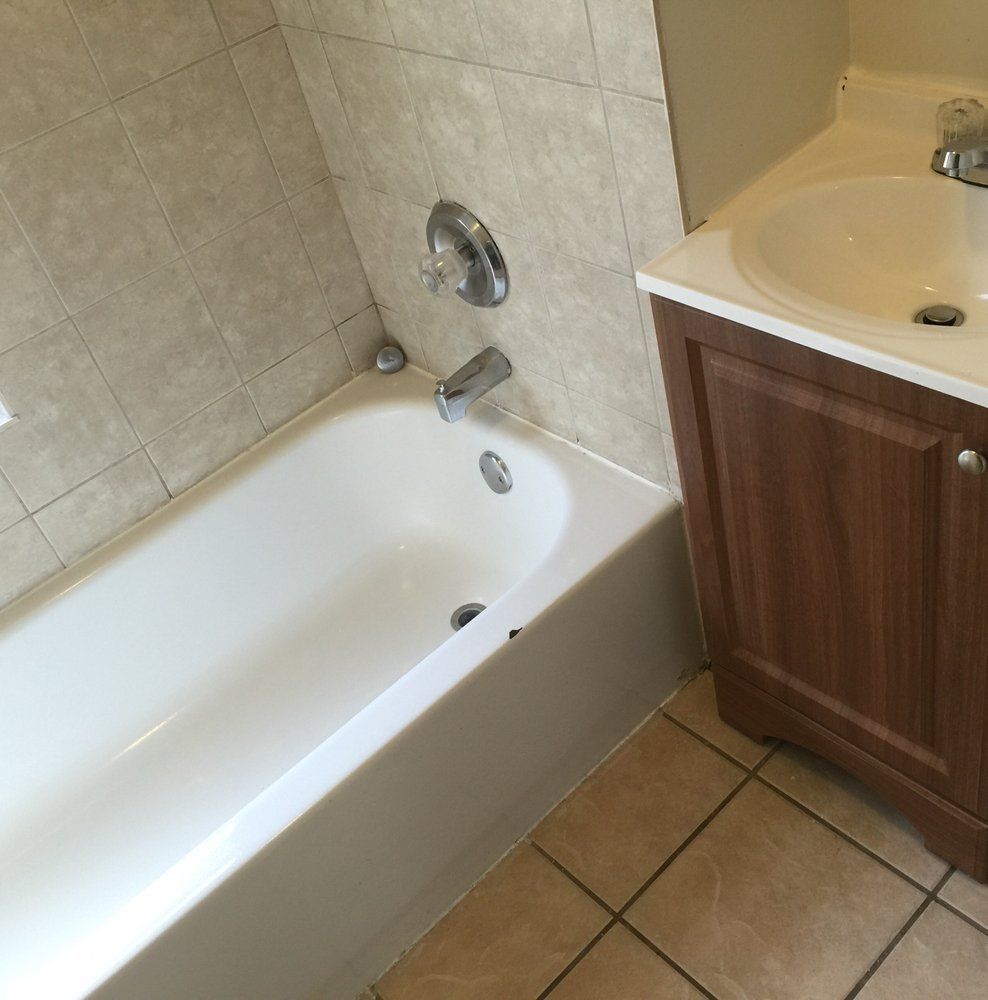Bathroom with white tub, beige tile walls, and a wood vanity beside it.