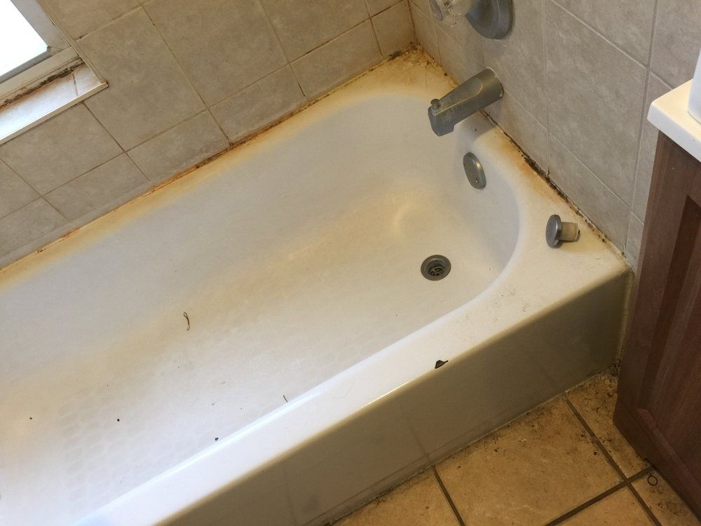 Dirty white bathtub with rust stains and a faucet in a tiled bathroom