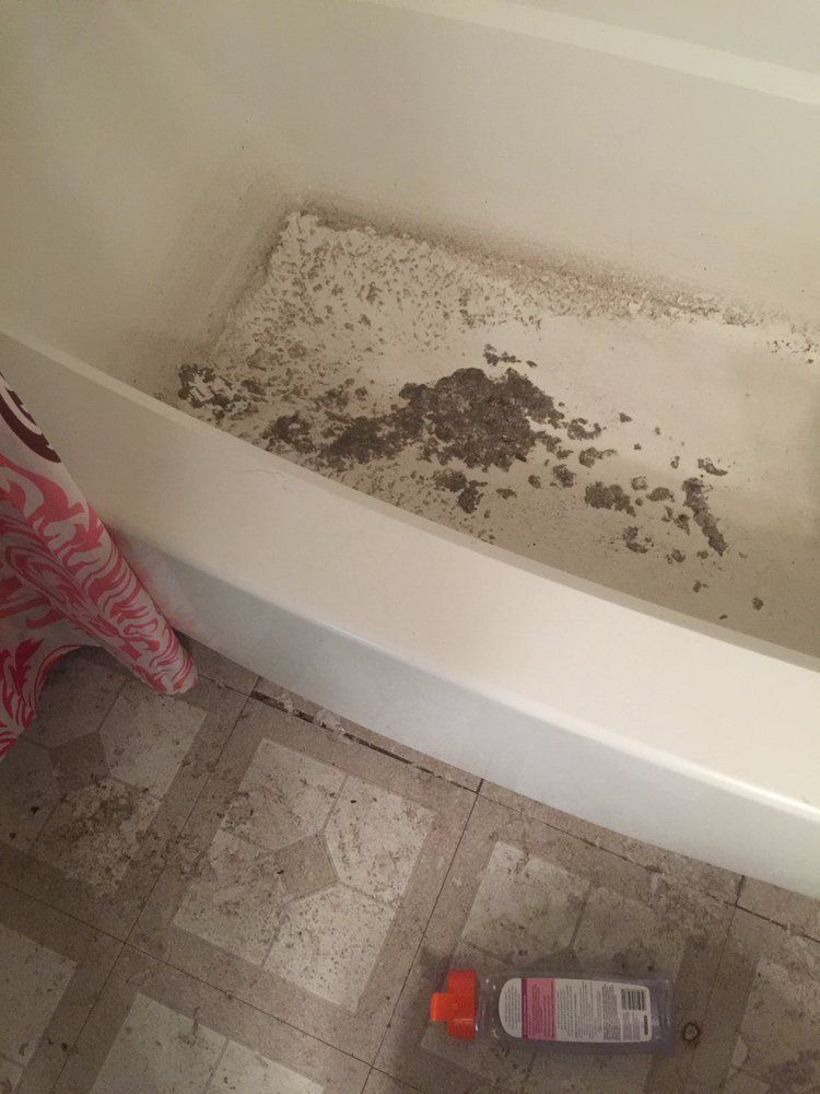 Dirty white bathtub with scattered dark debris and a bottle on patterned tile floor