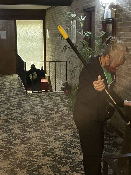 Person sweeping a carpeted hallway near a stairwell and potted plant