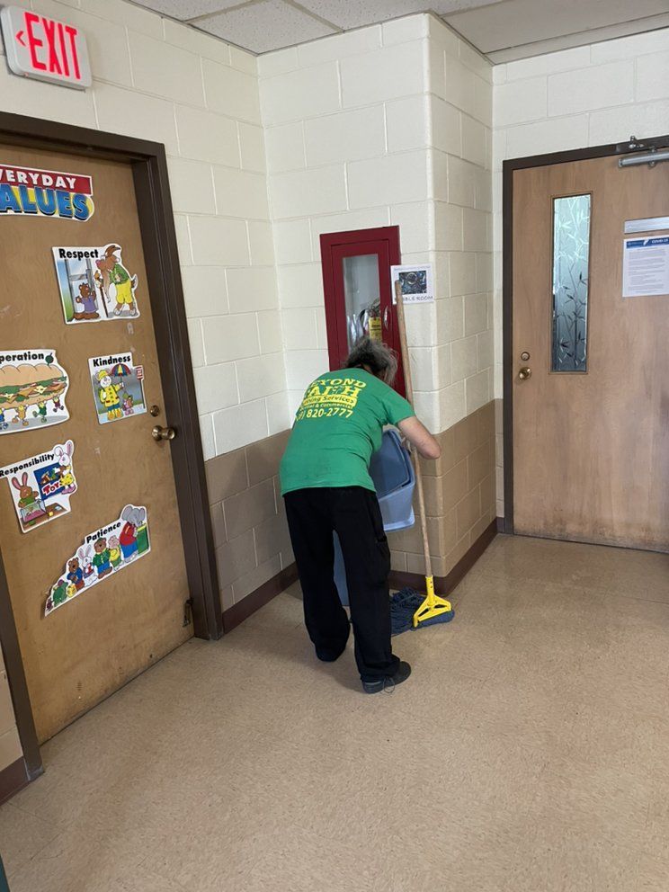 Person mopping a hallway beside classroom doors and an exit sign