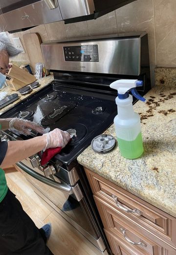 Person cleaning a black stovetop in a kitchen beside a granite countertop with a spray bottle.