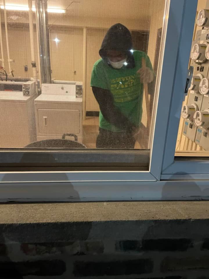 Person in a green shirt standing by a window inside a building.