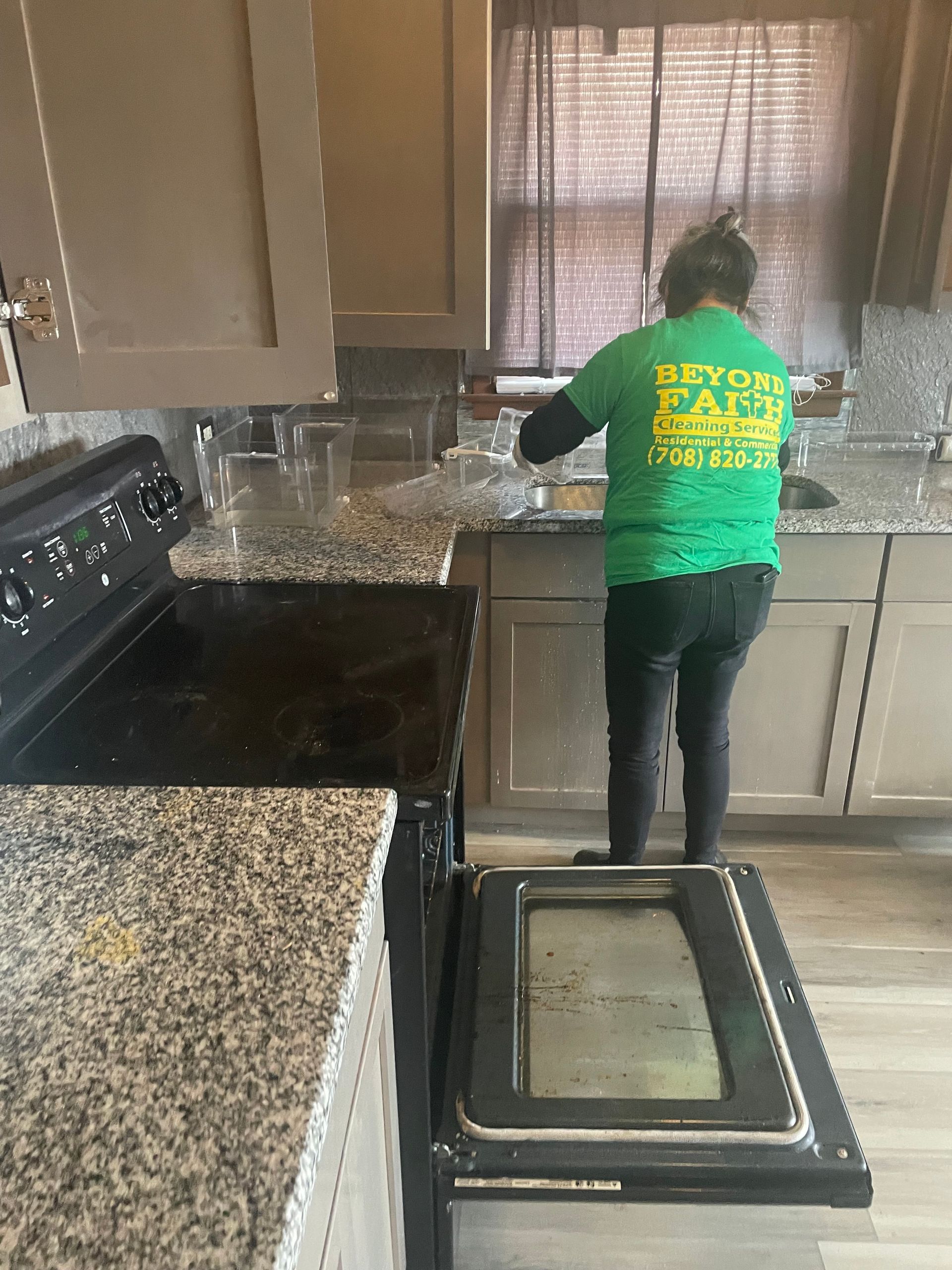 Person in a green shirt standing at a kitchen sink, cleaning dishes in a home kitchen.