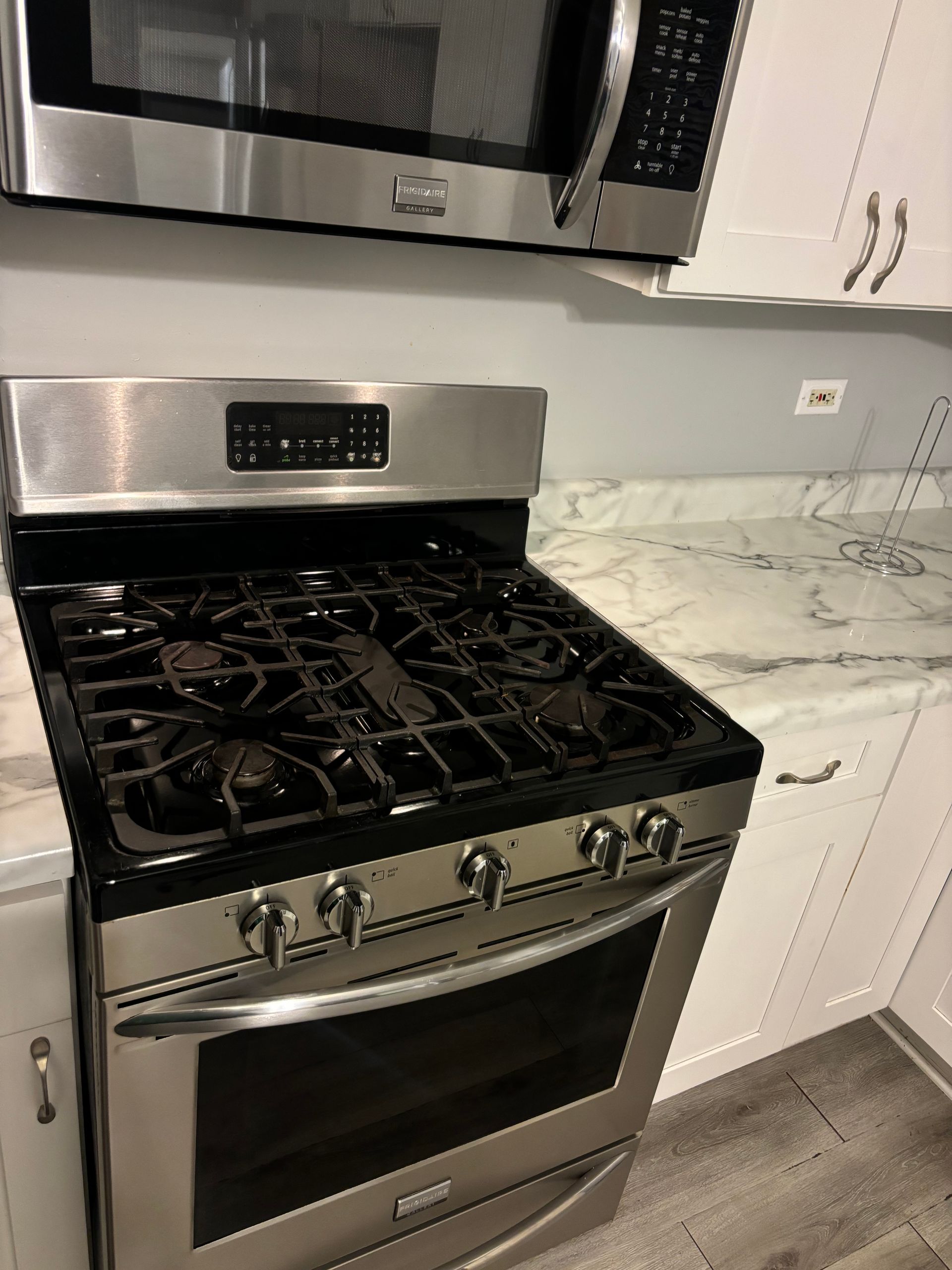Stainless steel gas range in a modern kitchen with white cabinets and marble-look countertops.
