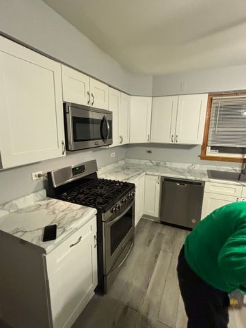 Modern white kitchen with marble counters, stainless steel appliances, and a person bending at the right edge.