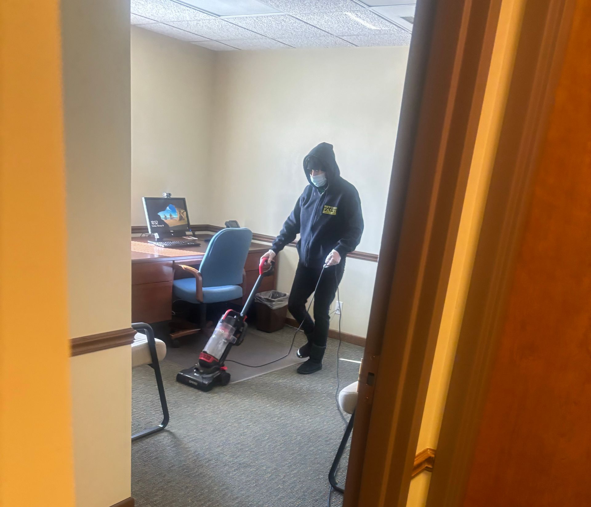 Person vacuuming an office carpet beside a desk and chair