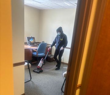 Person vacuuming an office carpet beside a desk and chair