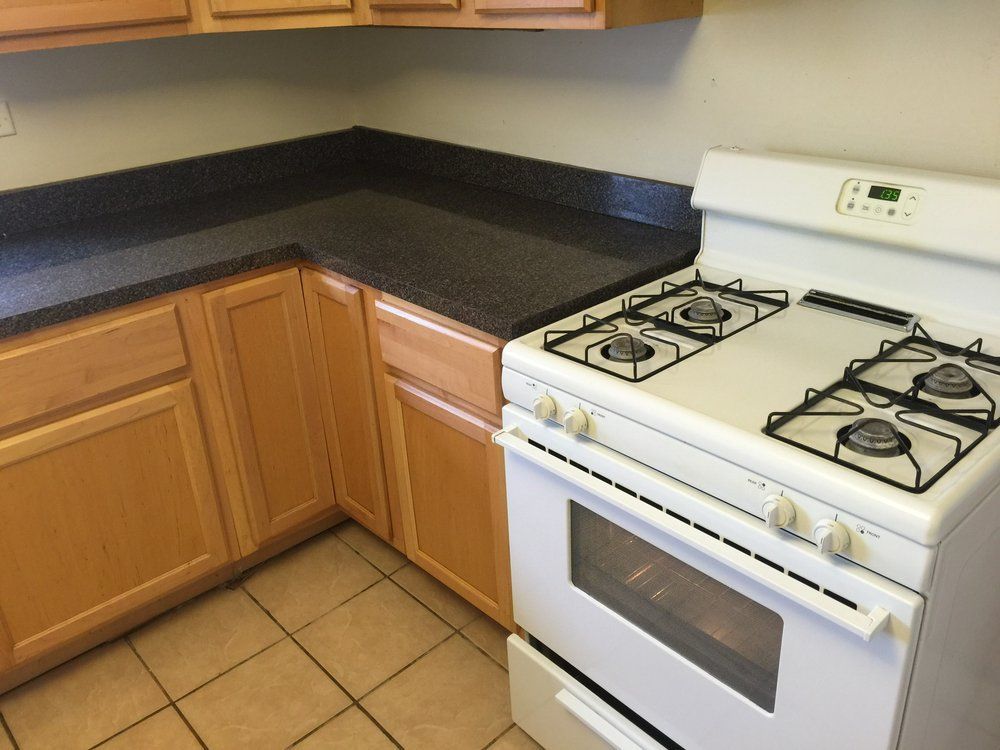 Small kitchen with wooden cabinets, black countertops, tile floor, and a white gas stove.