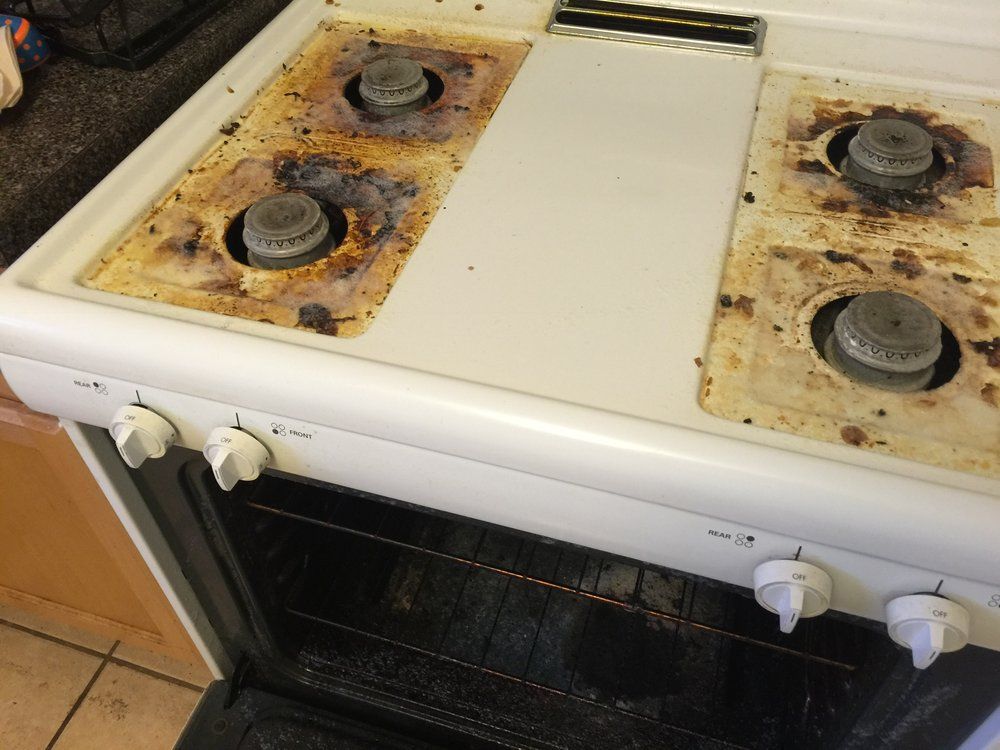 Dirty white gas stove with rusted burners and an open oven door in a kitchen