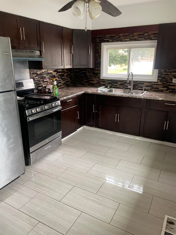 Modern kitchen with dark cabinets, stainless steel appliances, tiled backsplash, and a window over the sink