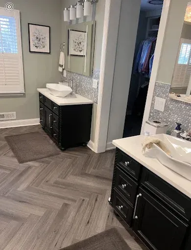 Bathroom with two black vanities, white sinks, mirrors, and herringbone tile flooring.