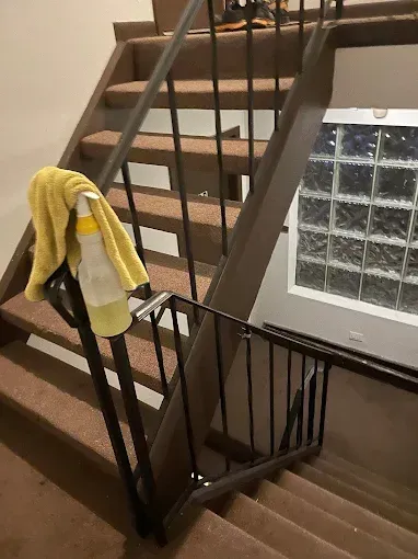 Apartment stairwell with brown carpet, black railings, and a yellow towel draped over the banister