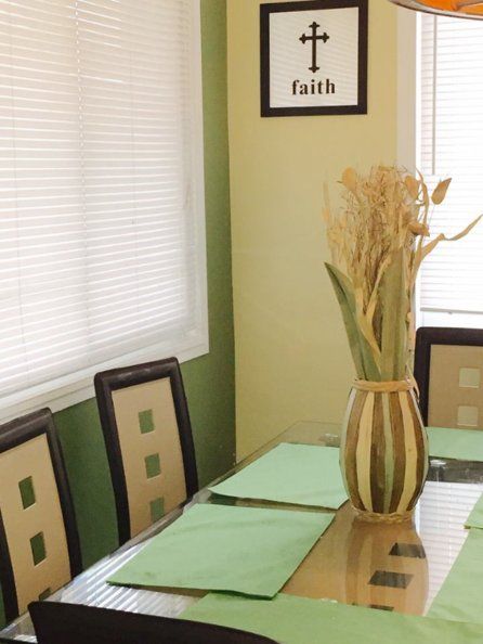 Dining room table with green placemats, vase of dried flowers, and a framed “faith” wall sign.