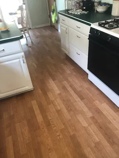 Bright kitchen with wooden floor, white cabinets, black stove, and a doorway at the far end.