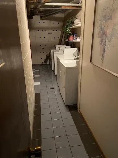 Narrow utility hallway with tiled floor, stacked laundry machines, shelves, and a wall map.