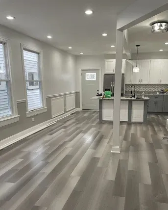 Bright open kitchen and living area with gray floors, white walls, and recessed lighting