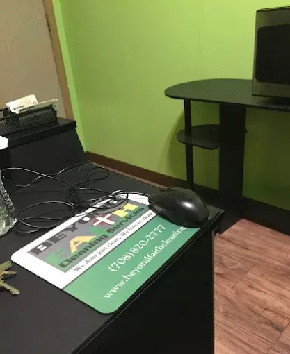 Black desk with cables, mouse, and green sign in a lime-walled office, with a side table in the corner.