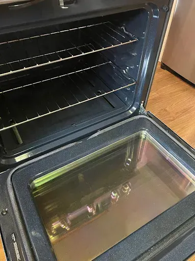 Open oven with racks and empty glass door, showing the dark interior and kitchen floor.