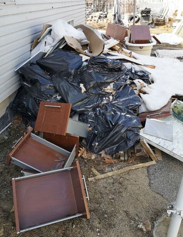 Piles of broken furniture and debris covered with black tarp beside a house in snow