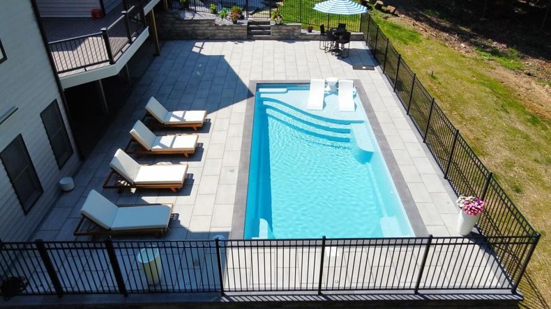 Backyard swimming pool with lounge chairs and patio, viewed from above through a black fence