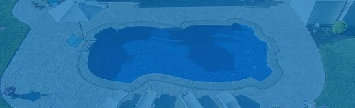 Blue-lit backyard swimming pool at night, with lounge chairs and a patio surrounding it.