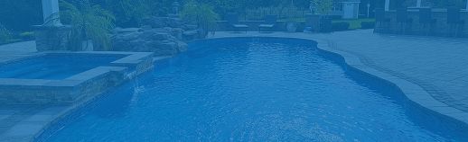 Blue-lit outdoor swimming pool at dusk with calm water and surrounding deck areas