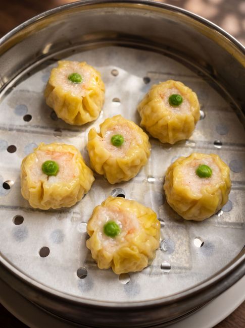 Six steamed dumplings with green garnish on a perforated metal steamer tray