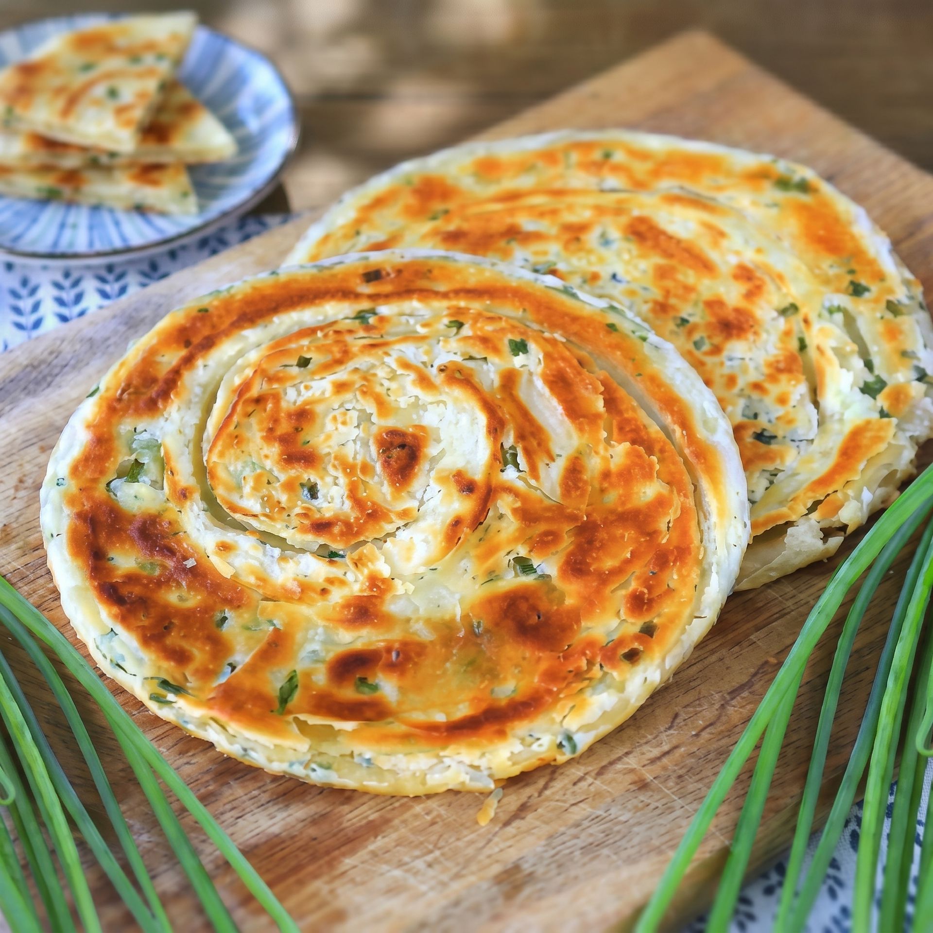 Golden fried flatbreads stacked on a wooden board, with chopped green onions nearby