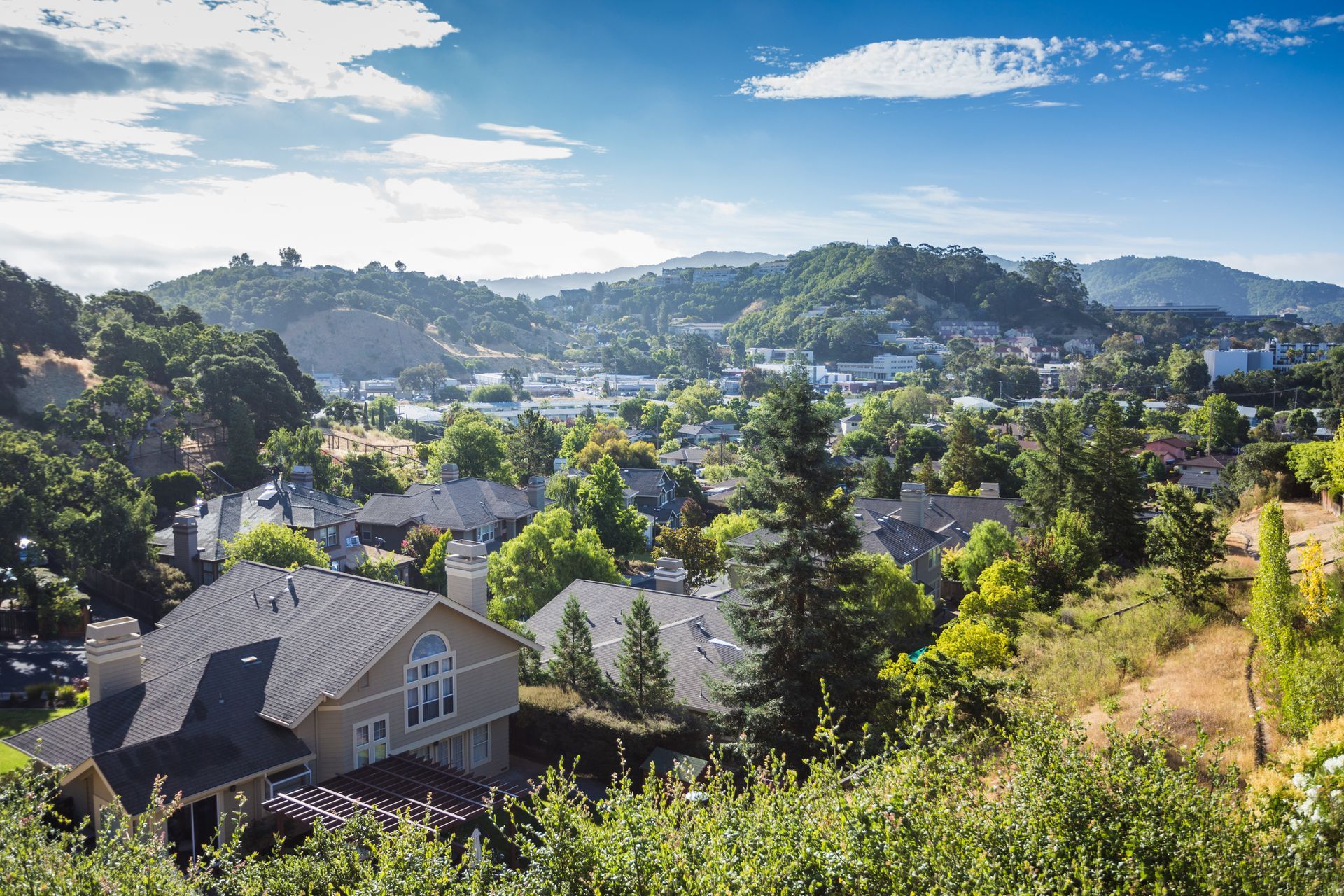A view of a residential area with a house in the foreground and mountains in the background.