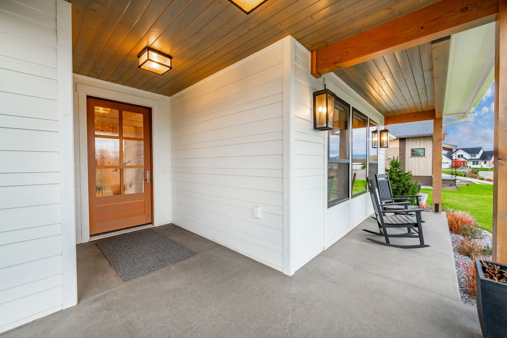 Covered front porch with white siding, wood ceiling, orange door, and a black chair by the window.