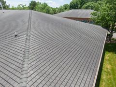 Gray shingled roof with vents, viewed from above, with trees and a house in the background