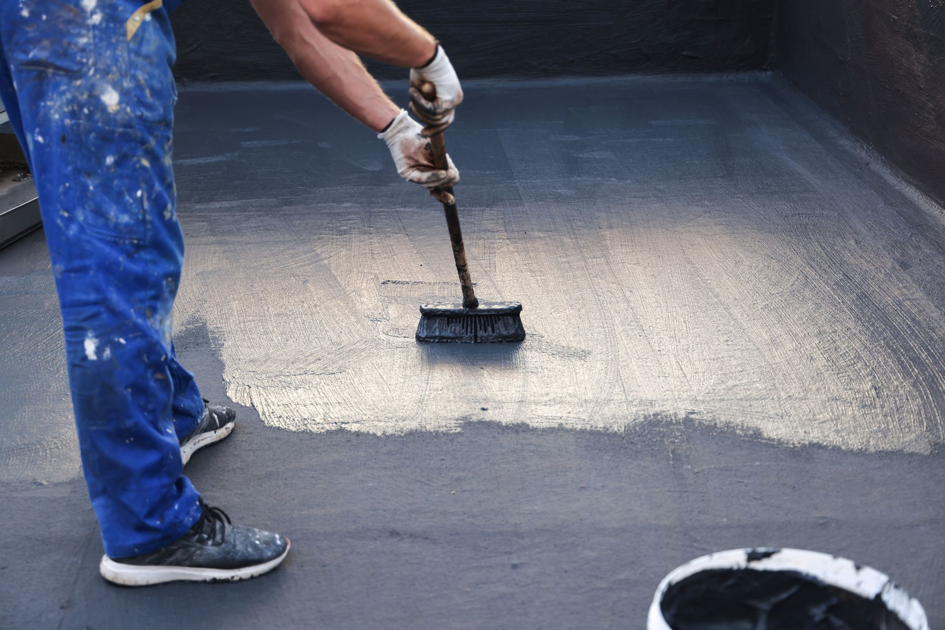 Worker painting a dark surface with a brush in a large container or truck bed