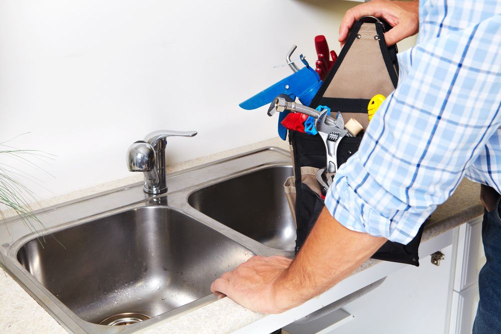 A Man is Fixing a Kitchen Sink With a Tool Bag Full of Tools — Dave's Plumbing and Gasfitting in Maroochydore, QLD