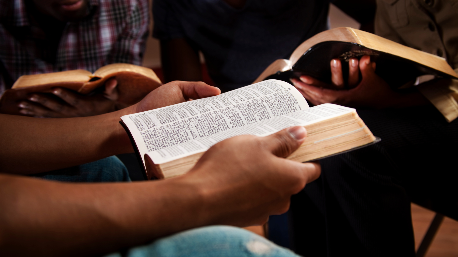 Hands holding open books and a Bible during a small group reading session.