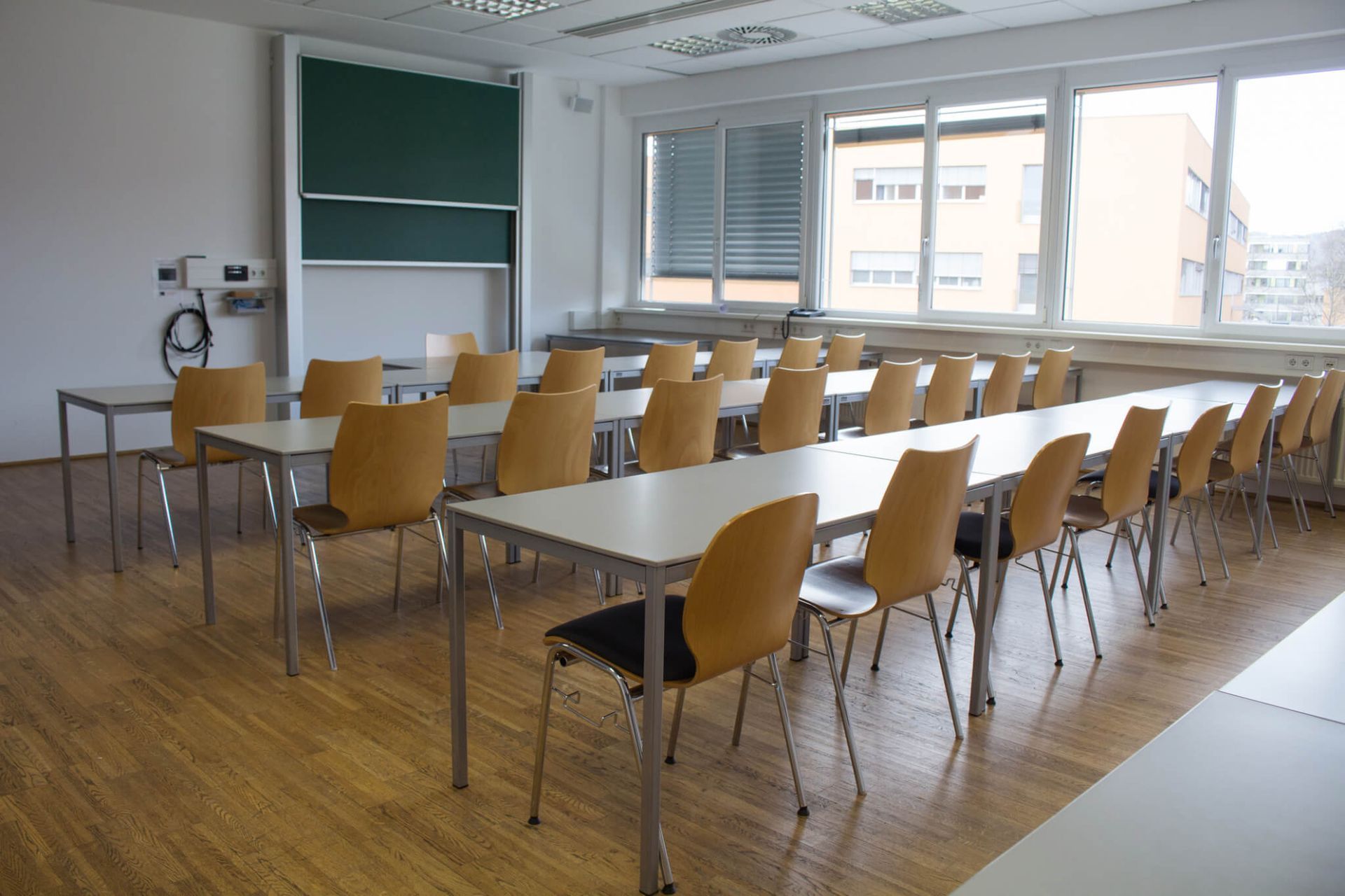 A classroom with tables and chairs and a green board