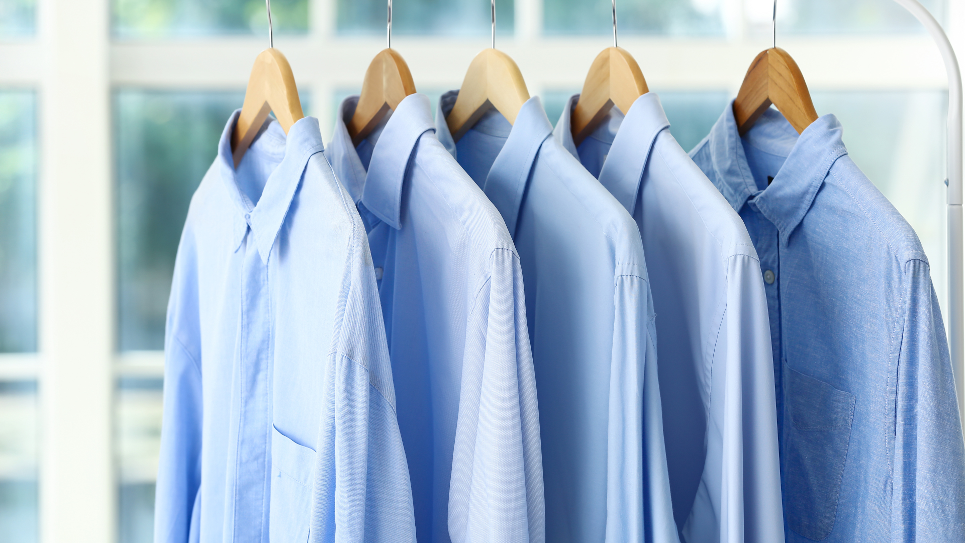 A row of blue shirts hanging on a rack.