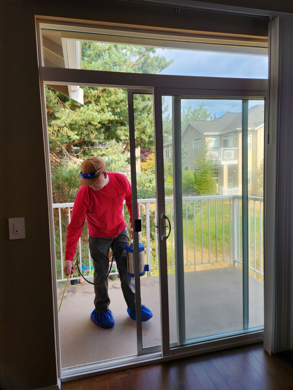 Worker in red shirt and blue boot covers adjusting a sliding glass door on a patio