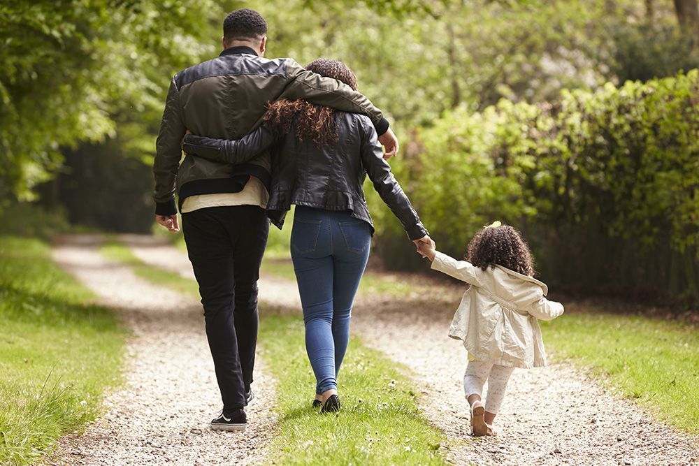 Family walks down a path, parents with arms around each other, child holding a hand, outdoors.