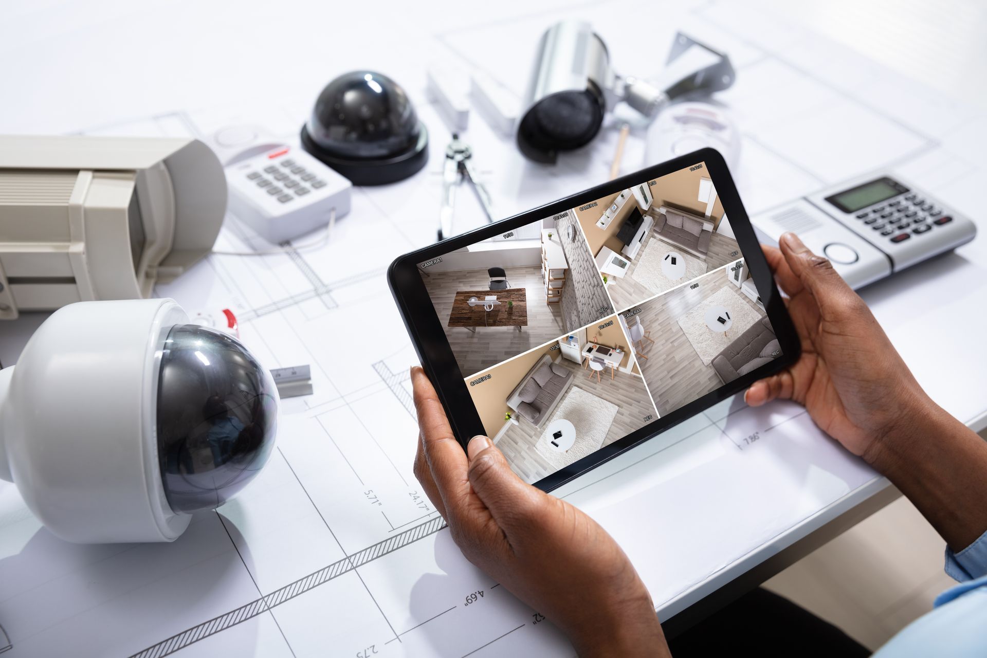 A technician viewing live home security camera feeds on a tablet over blueprints.