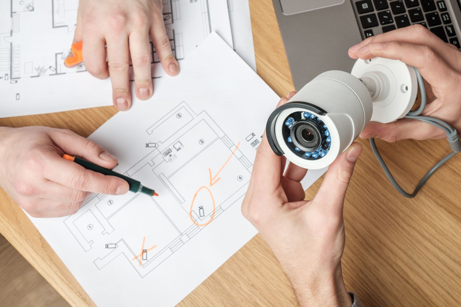 A man is holding a security camera over a drawing of a house.