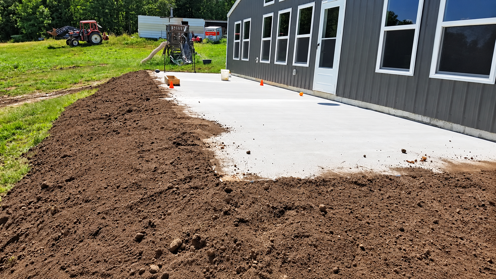 Fresh concrete patio beside a gray building, bordered by brown mulch in a yard
