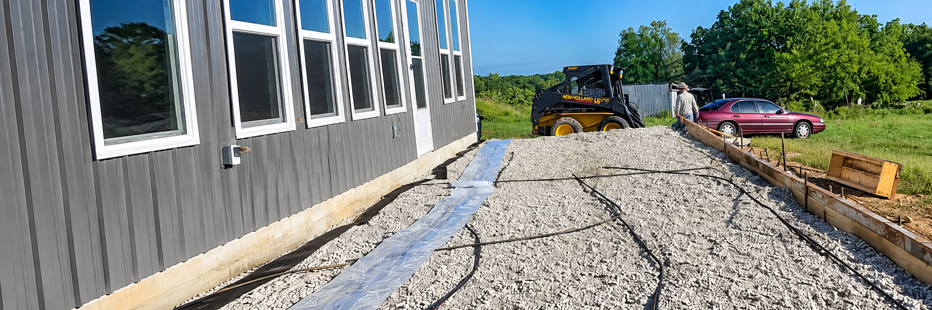 Gravel walkway alongside a gray building, with windows and construction materials in the background