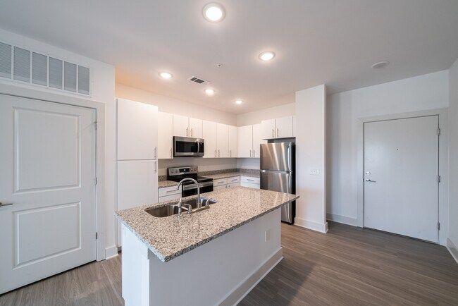 Modern white kitchen with island, stainless steel appliances, and wood-look flooring.