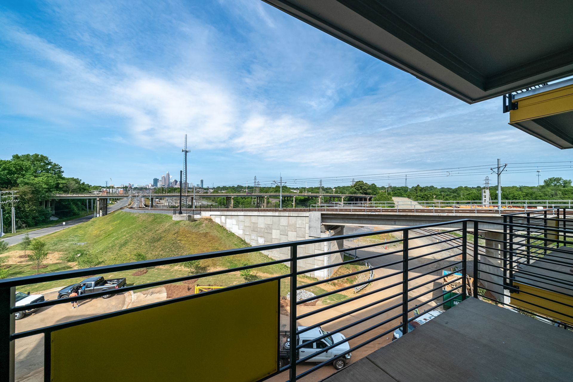 Balcony view of elevated train tracks, highway, and cityscape under a blue sky.