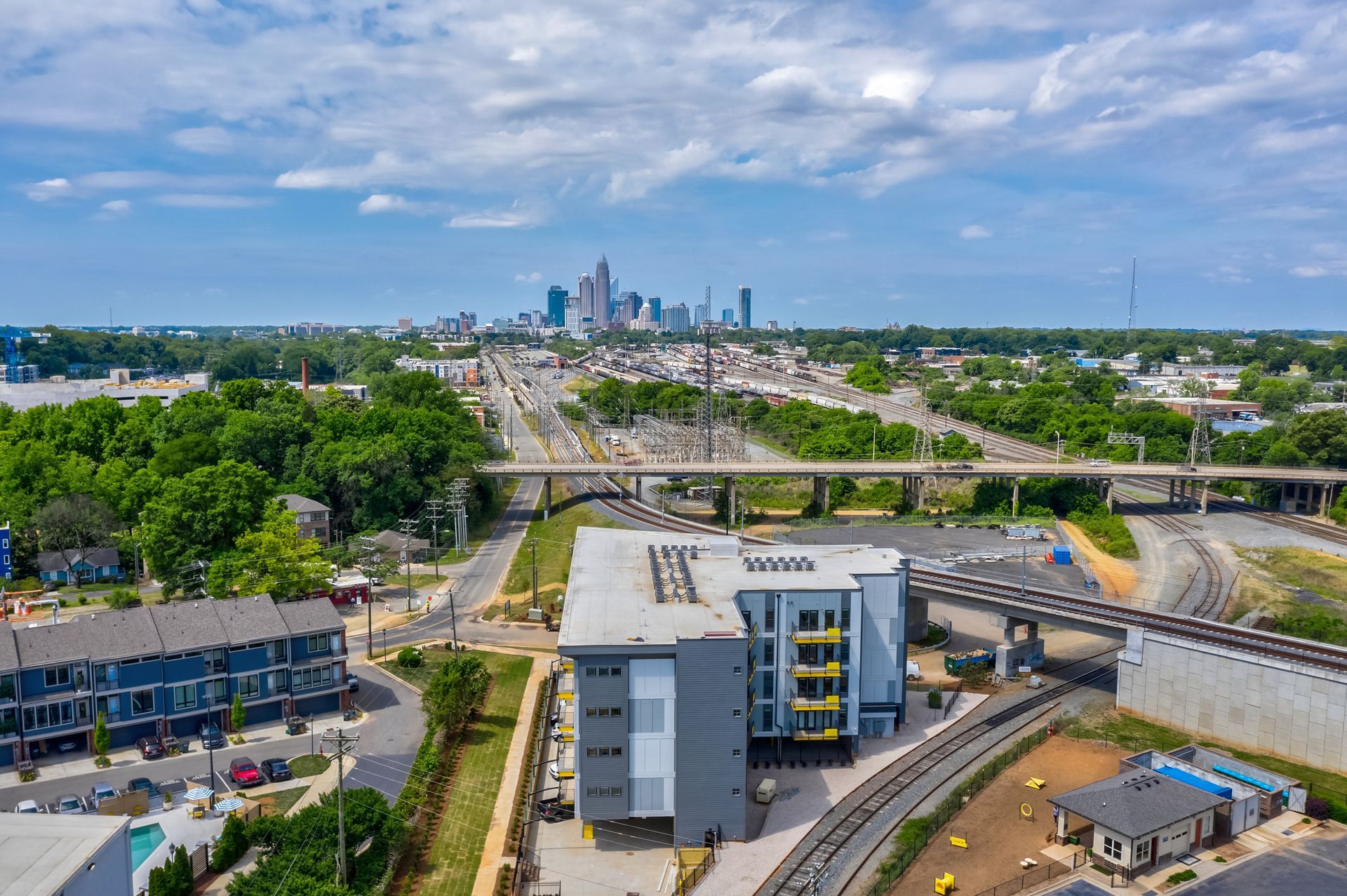Aerial view: Modern apartment building near train tracks, with Charlotte, NC skyline in the background.