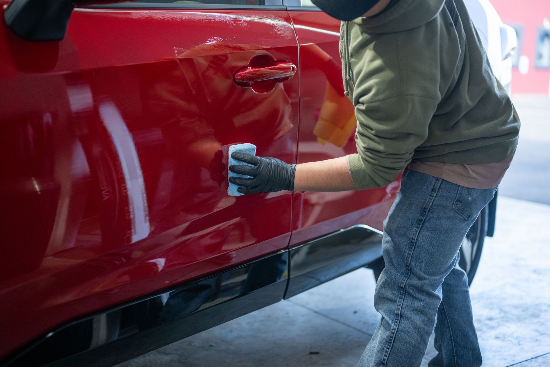 Person polishing a red car door with a cloth in a garage.