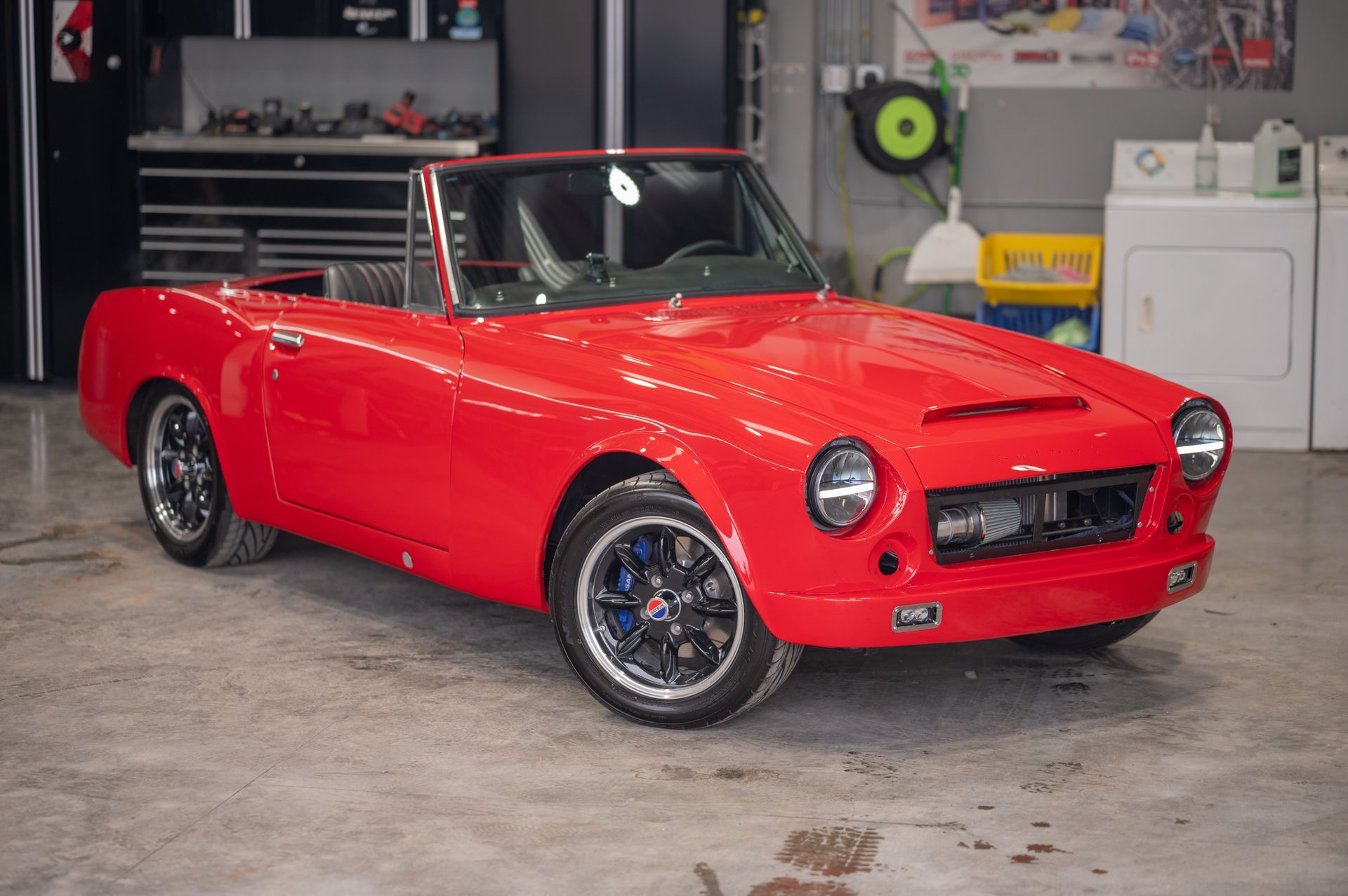 Red vintage convertible sports car in a garage, bright red with black wheels and chrome trim